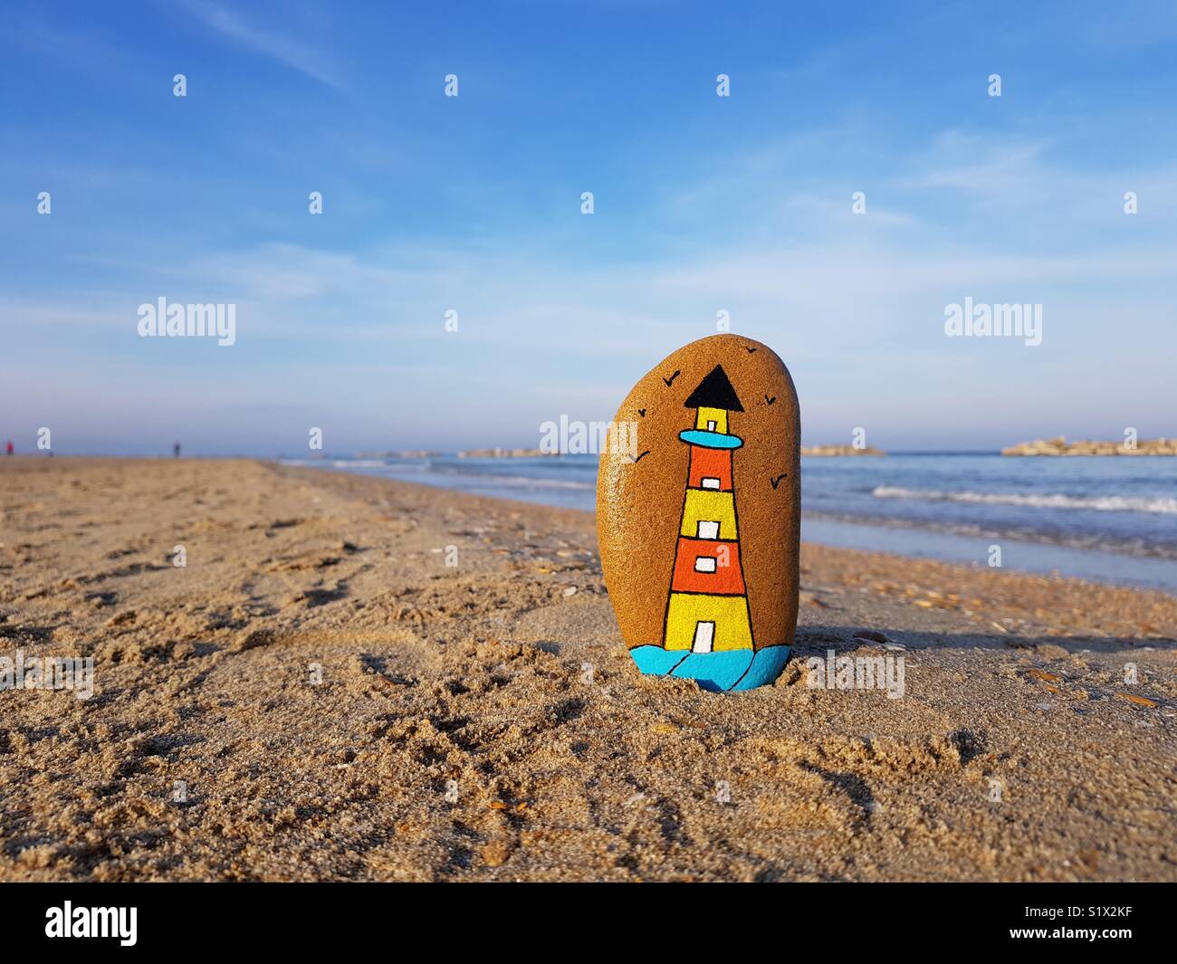 Lighthouse concept with a painted stone on the beach - Smartphone Captured Stock Image