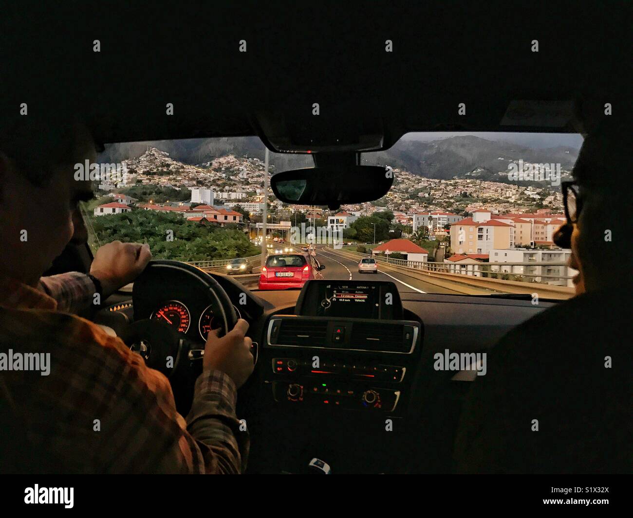 View through car windscreen to the road ahead from the back seat, with driver and passenger in silhouette, at dusk - Smartphone Captured Stock Image