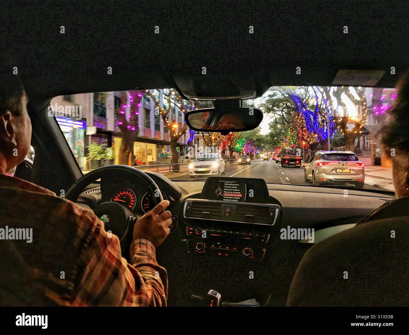 View through car windscreen to the road ahead from the back seat, with Christmas lights in the city at dusk, Funchal, Madeira, Portugal - Smartphone Captured Stock Image