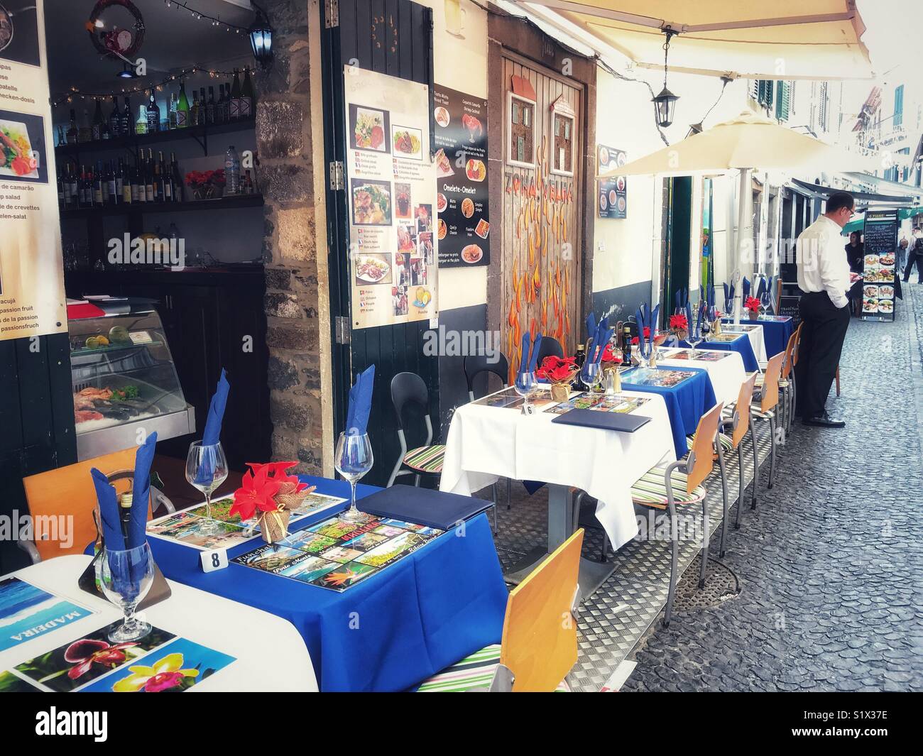 Street scene with a restaurant, showing the painted doors art project in the rejuvenated historic Rua Santa Maria, Saint Maria Street, Funchal, Madeira, Portugal - Smartphone Captured Stock Image
