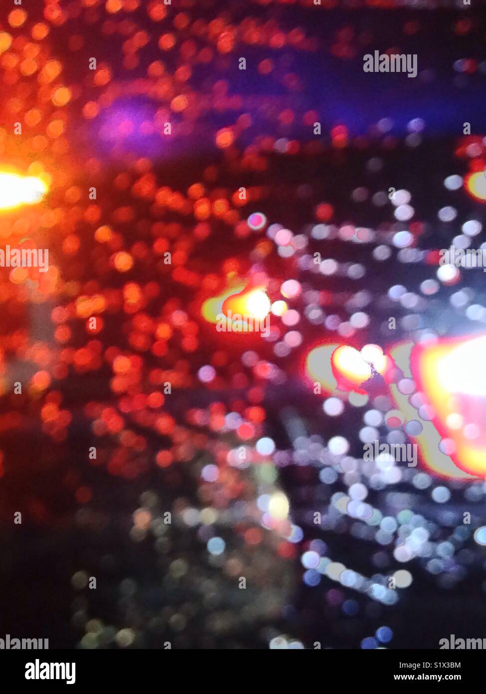 Emergency vehicle flashing lights through a rainy car window. Abstract effect. Stock Photo