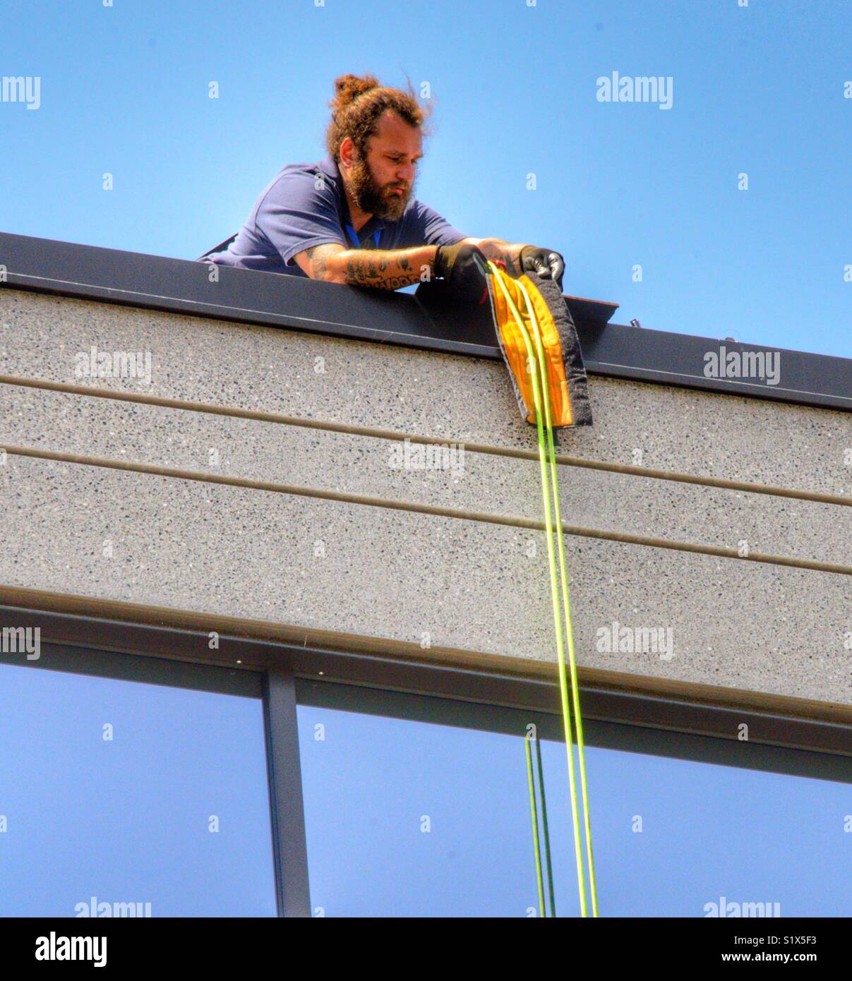 Man who is a window washer is setting up his rigging to prepare to rappel down the side in order to wash windows Stock Photo
