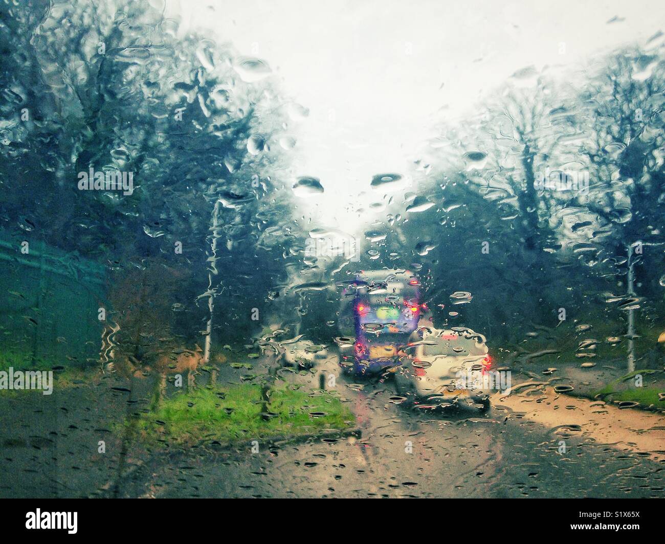 Looking out through a car windscreen covered in raindrops in rainy weather. Stock Photo