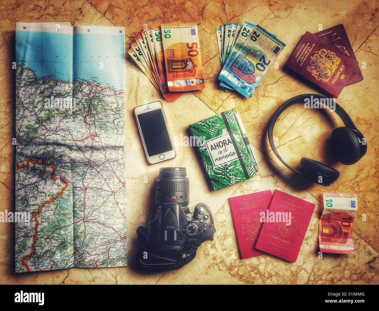 Flatlay photography, travel items including map, passports, DSLR camera, Beat headphones, notebooks, iPhone, and euros. Stock Photo