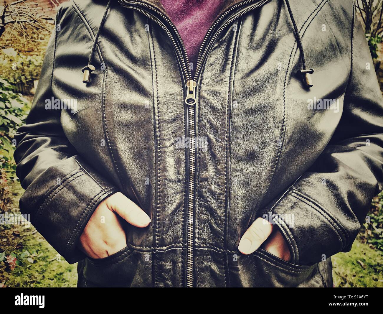 Woman outdoors, wearing brown leather jacket, hands in pockets, midsection - Smartphone Captured Stock Image