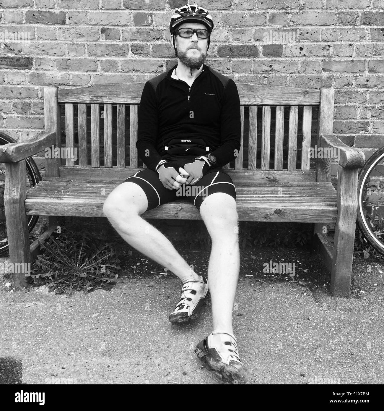 A cyclist takes a break on a bench in a village in England - Smartphone Captured Stock Image