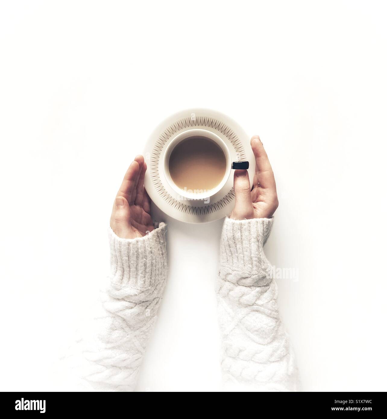 Looking down from above onto a white background with a girl’s hands holding a cup of tea in a cup and saucer - Smartphone Captured Stock Image
