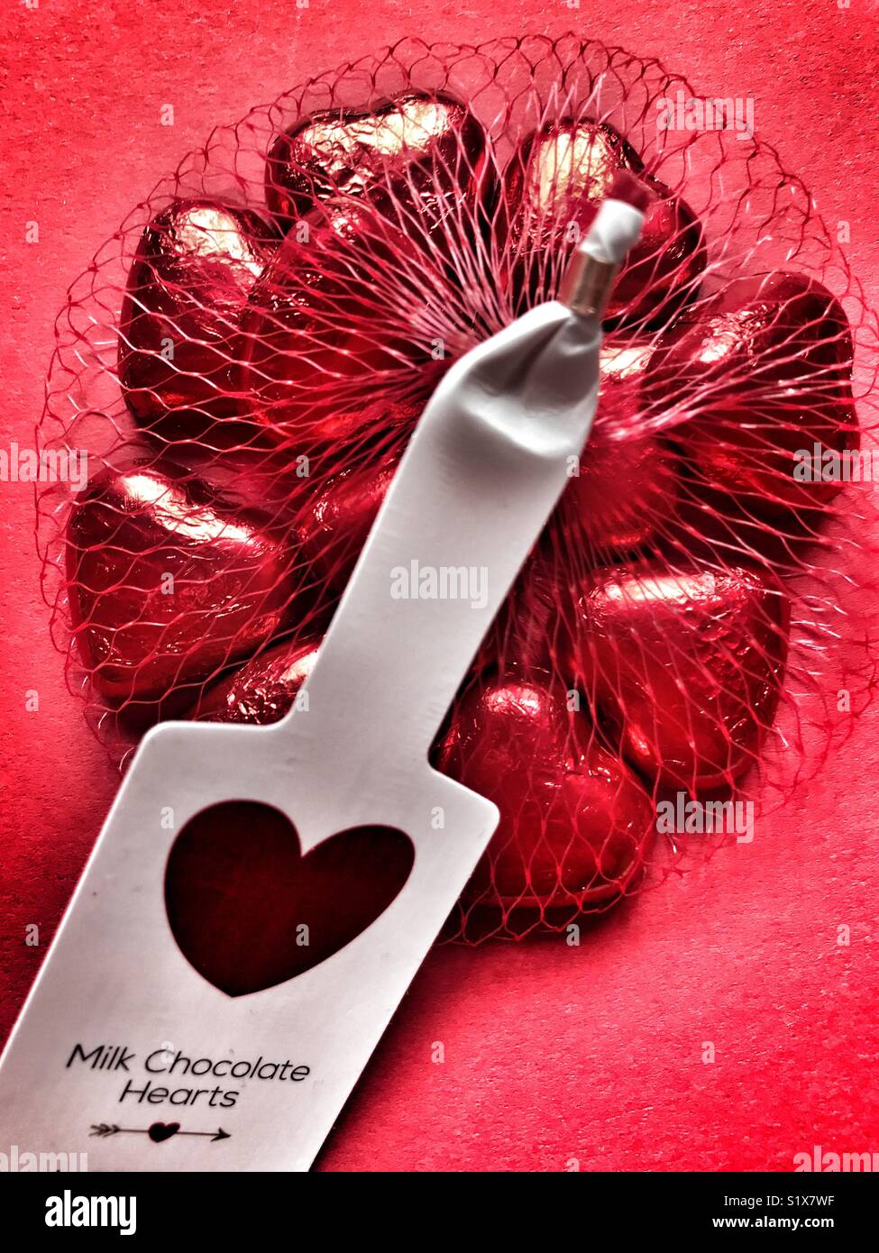 Valentine’s Day treat. Milk chocolate hearts wrapped in red foil, in a red plastic net bag - Smartphone Captured Stock Image