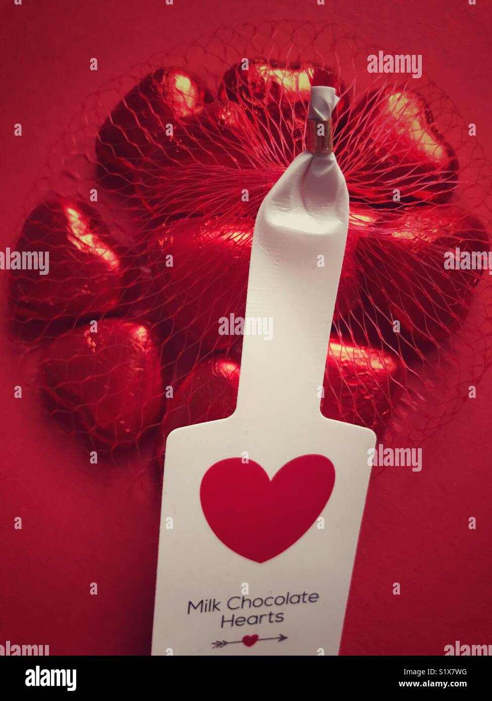 Valentine’s Day treat. Milk chocolate hearts wrapped in red foil, in a red plastic net bag - Smartphone Captured Stock Image