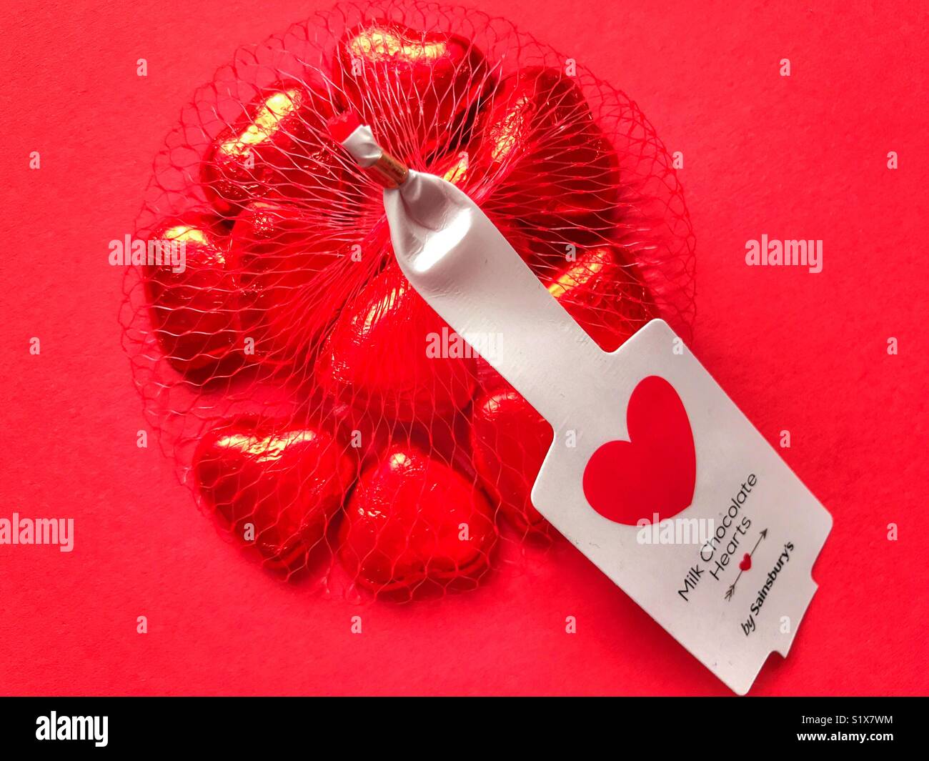 Valentine’s Day confectionery from Sainsbury’s. Milk chocolate hearts wrapped in red foil, in a red plastic net bag - Smartphone Captured Stock Image
