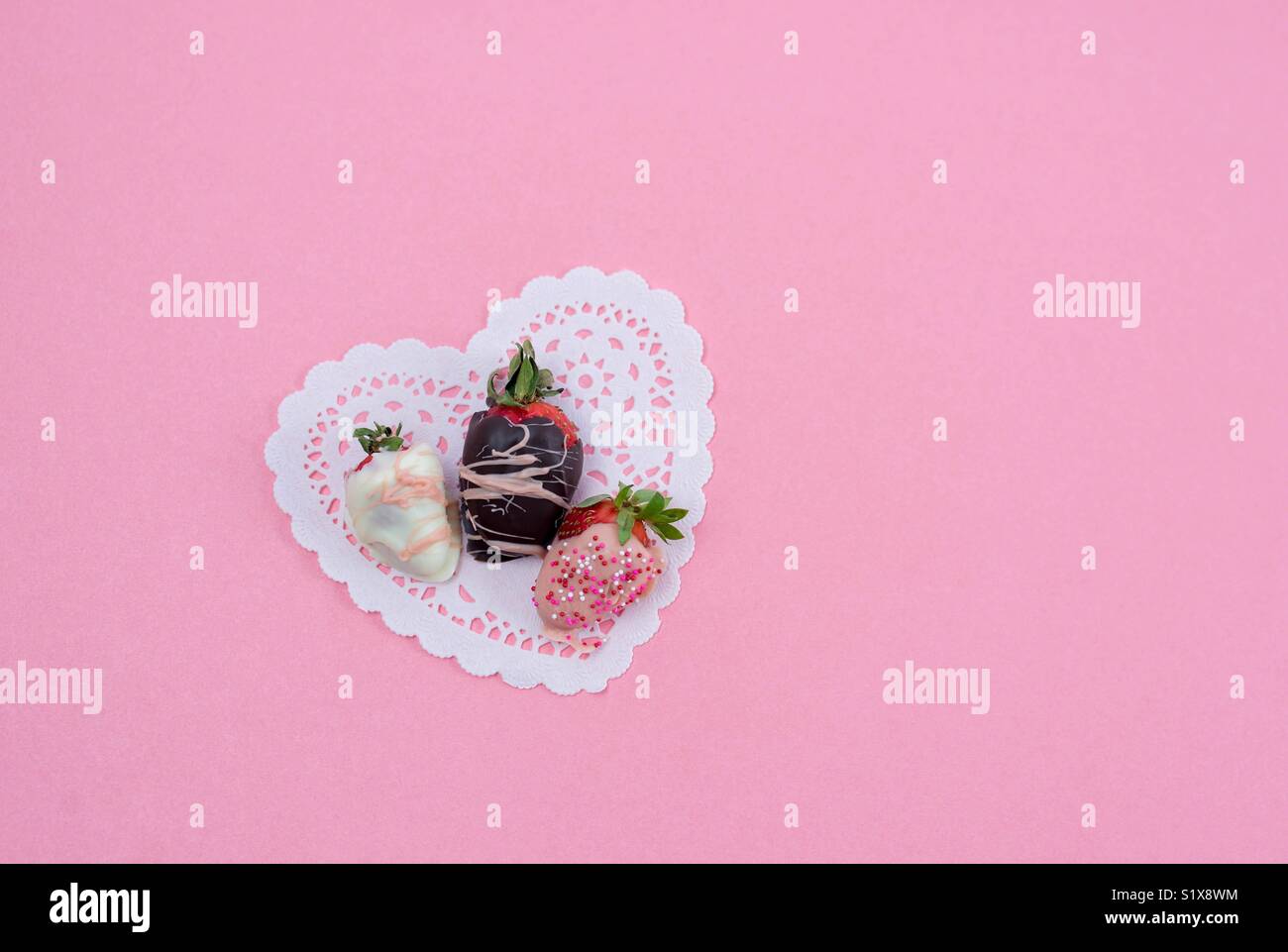 Chocolate dipped strawberries on heart shaped paper doily on pink background with space for copy Stock Photo