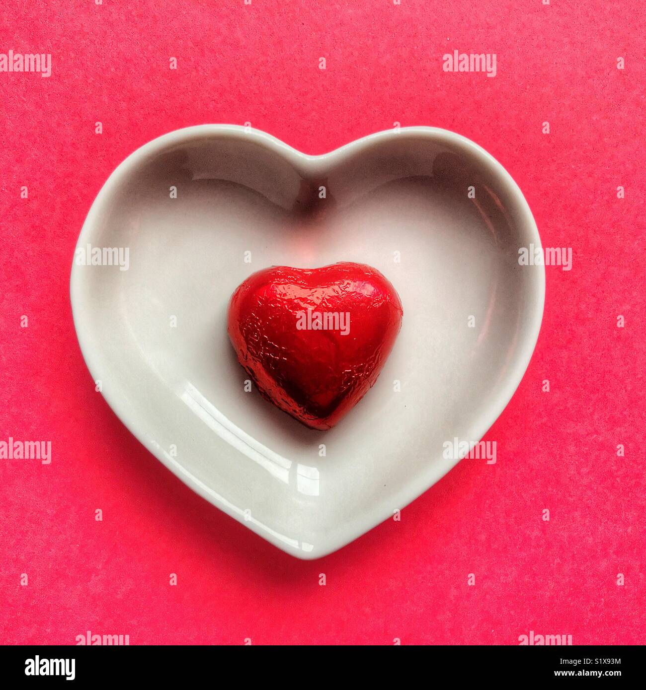 Red heart shaped chocolate in a white ceramic dish on a red background - Smartphone Captured Stock Image