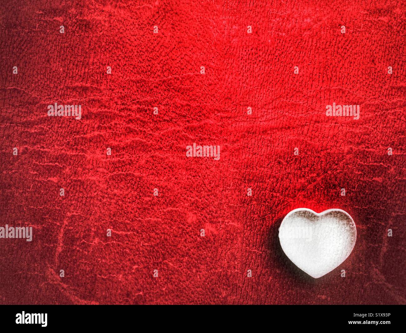 Flatlay photography. Heart shaped white ceramic dish, on red, symbol of love on Valentine’s Day - Smartphone Captured Stock Image