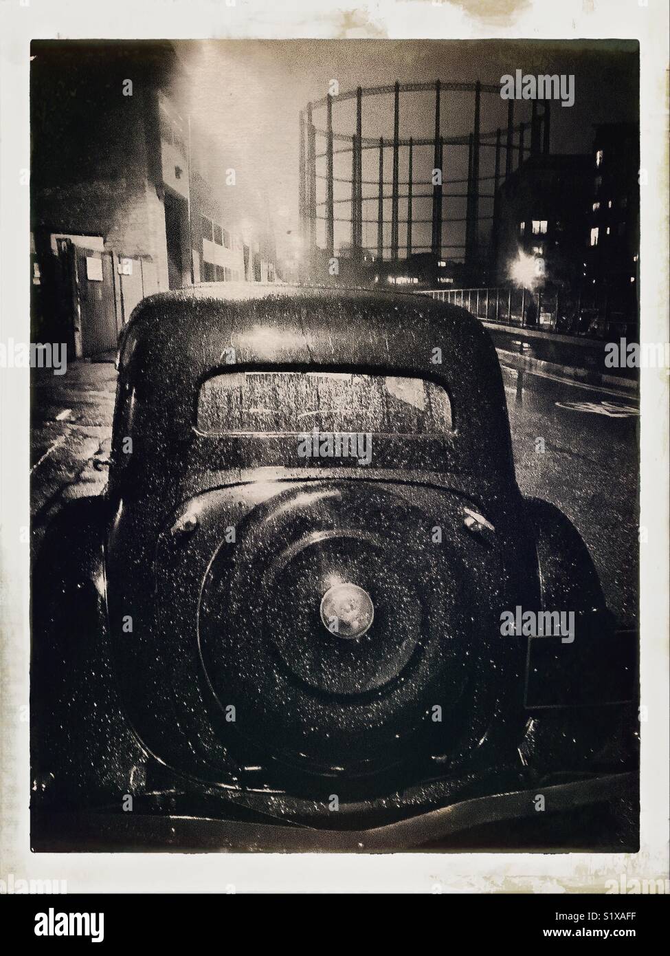 Night scene and a vintage car In east London and Victorian gasometer in the background. Photo edited to give it a vintage look. - Smartphone Captured Stock Image