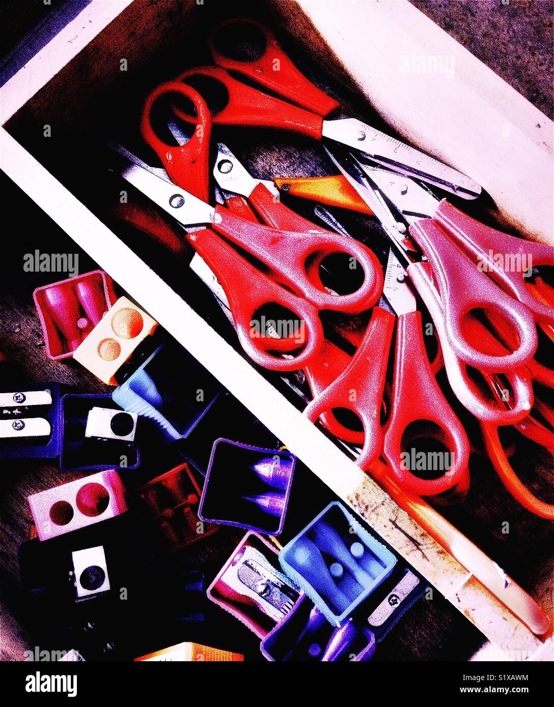 Box of red handled scissors and coloured pencil sharpeners Stock Photo