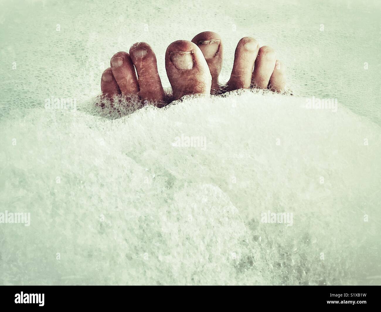 Female toes sticking out of foamy bubble bath bubbles processed in a creative grunge style to give a creepy feel - Smartphone Captured Stock Image