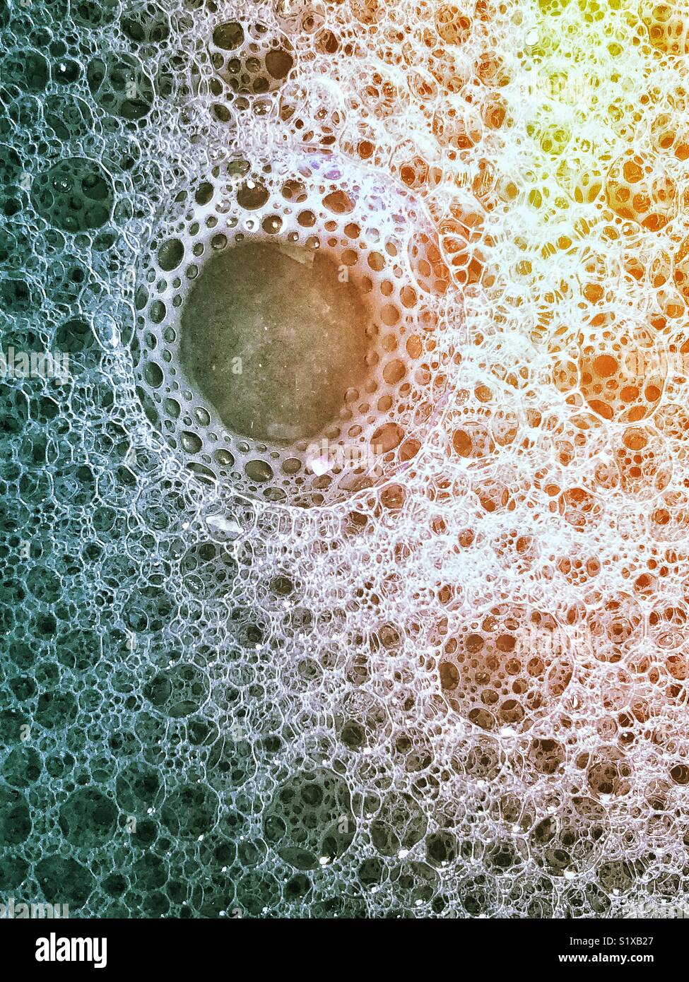 Closeup of large clear bubble surrounded by small and medium bubbles in a bubble bath with rainbow lighting effect Stock Photo