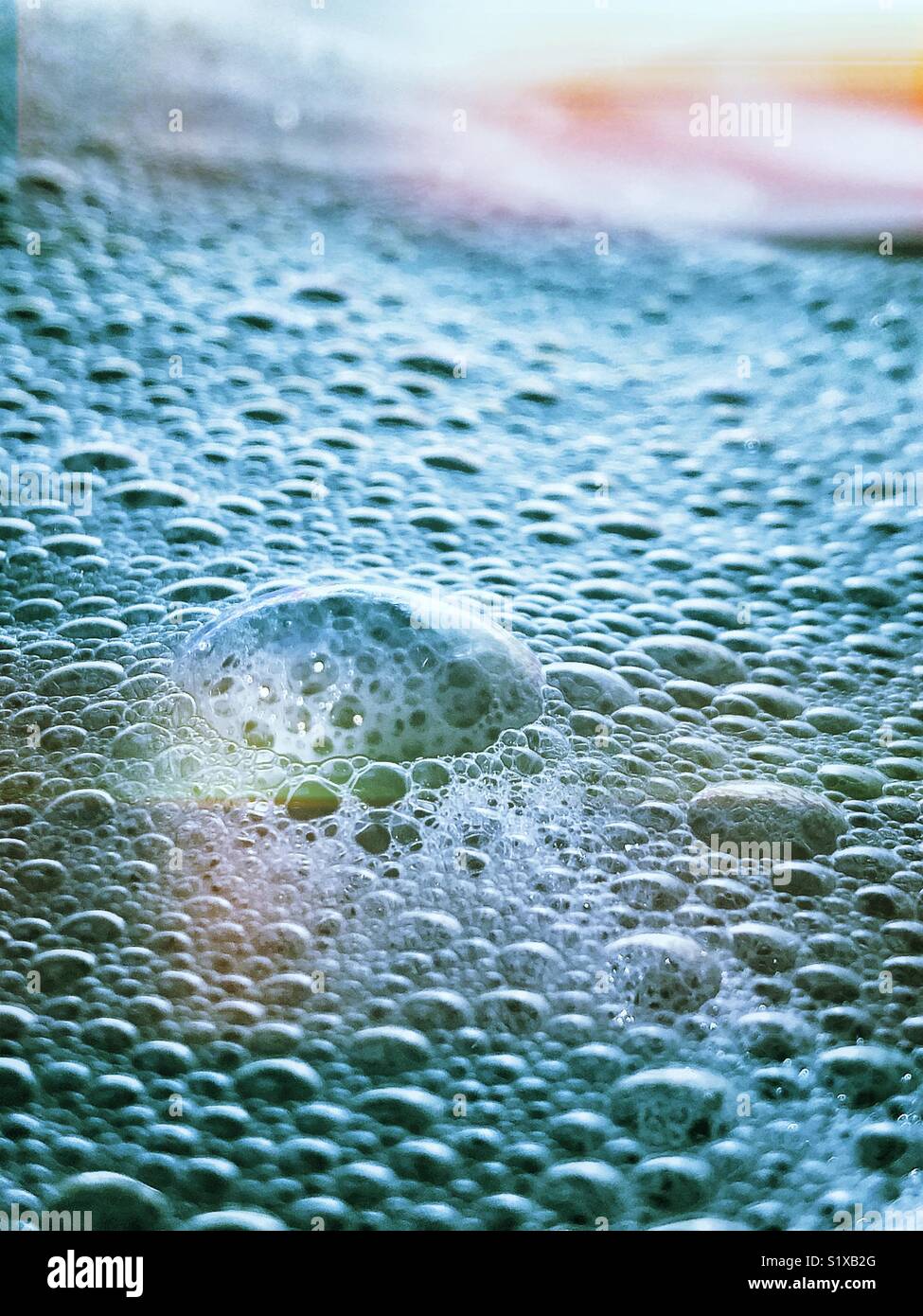 Closeup of large clear bubble amidst a sea of blue tinted bubbles in a bubble bath with rainbow lighting effect - Smartphone Captured Stock Image