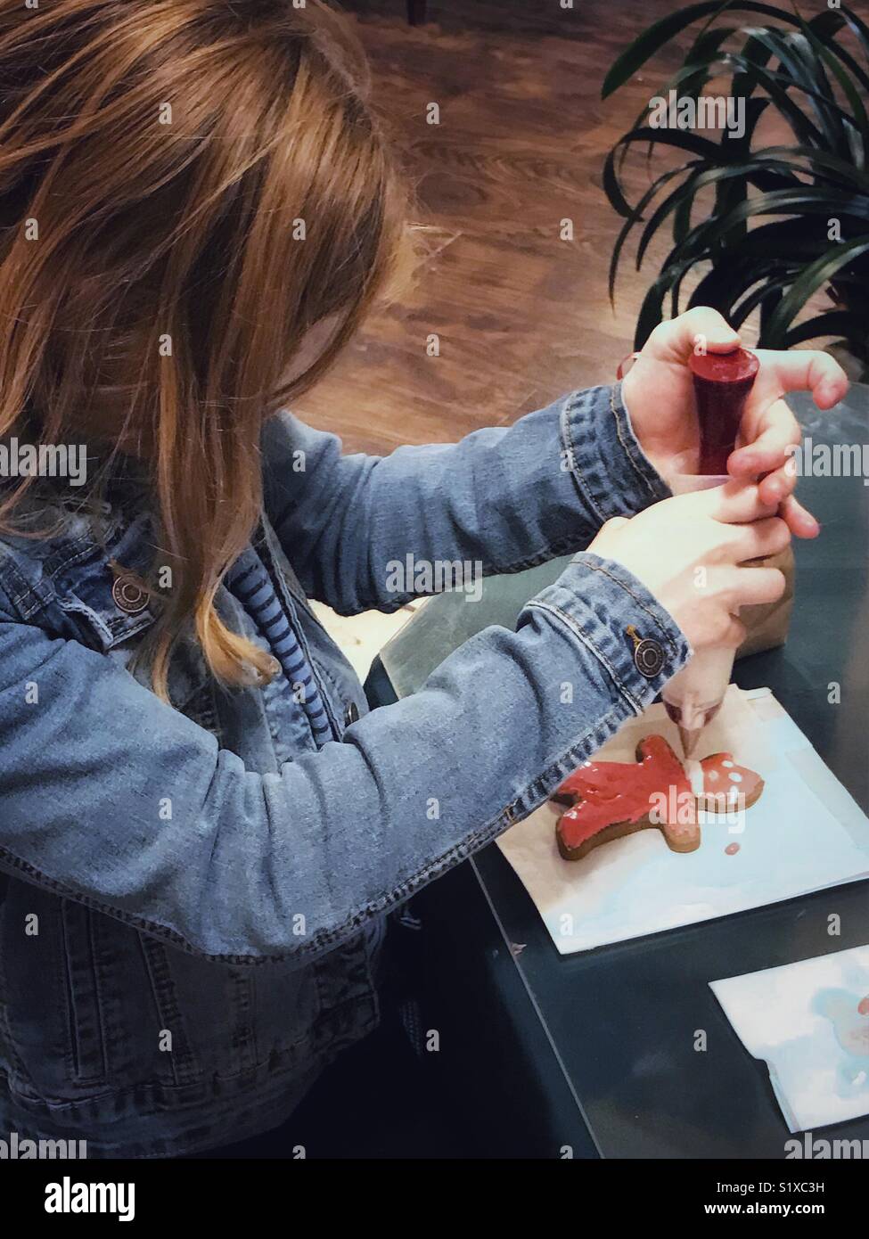 A girl decorates a gingerbread man already missing a bite from its head. - Smartphone Captured Stock Image