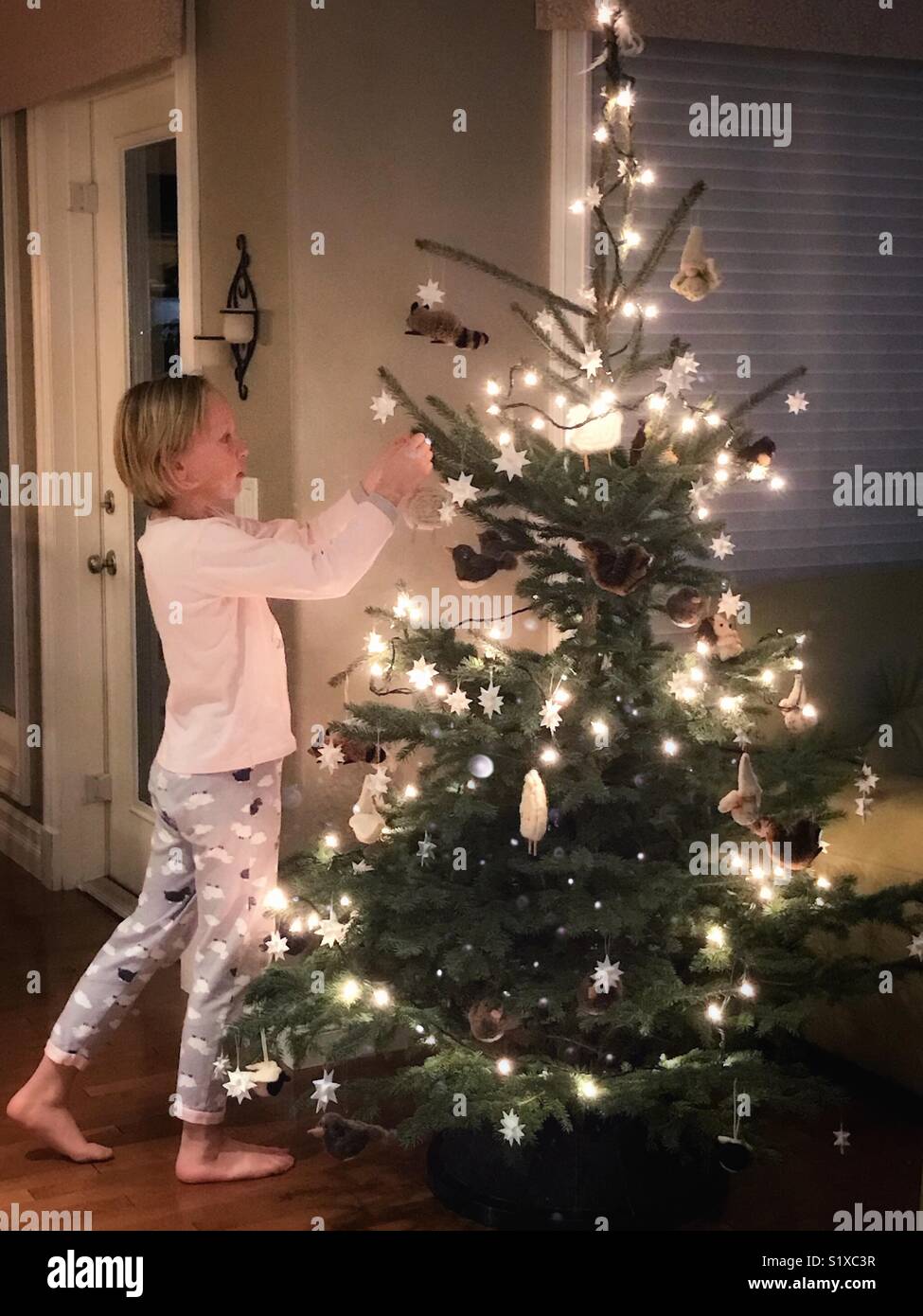 A girl wearing pyjamas decorates a Christmas tree. Stock Photo
