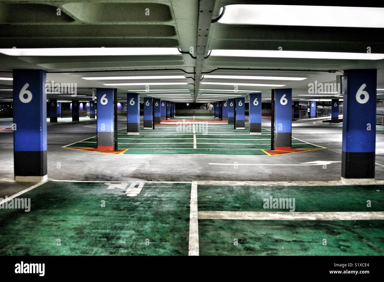 The interior of level 6 of a deserted multi story car park with harsh lights illuminating colourful parking spaces and columns Stock Photo