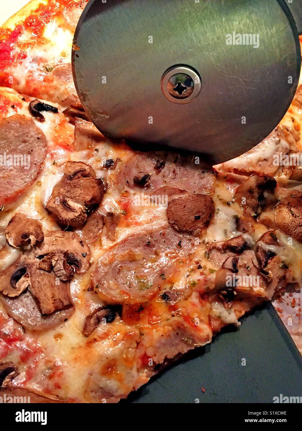 Metal cutting wheel slicing through sausage and mushroom pizza - Smartphone Captured Stock Image