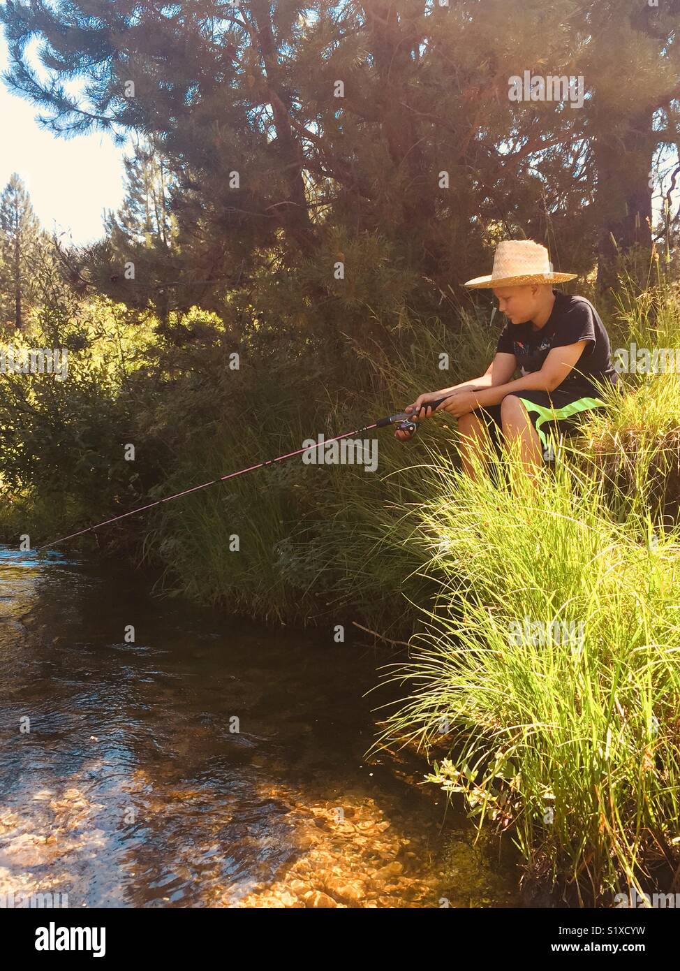 Young boy wearing a straw hat and fishing from the river bank Stock Photo -  Alamy