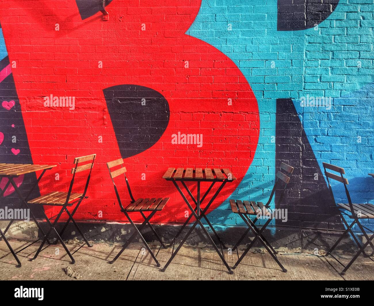 Empty cafe tables and chairs in front of bold graffiti in brooklyn New York - Smartphone Captured Stock Image