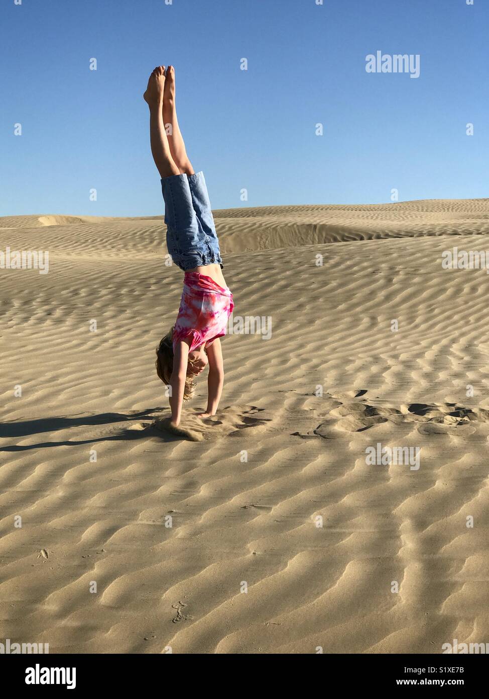 A girl does a handstand on a sand dune. - Smartphone Captured Stock Image