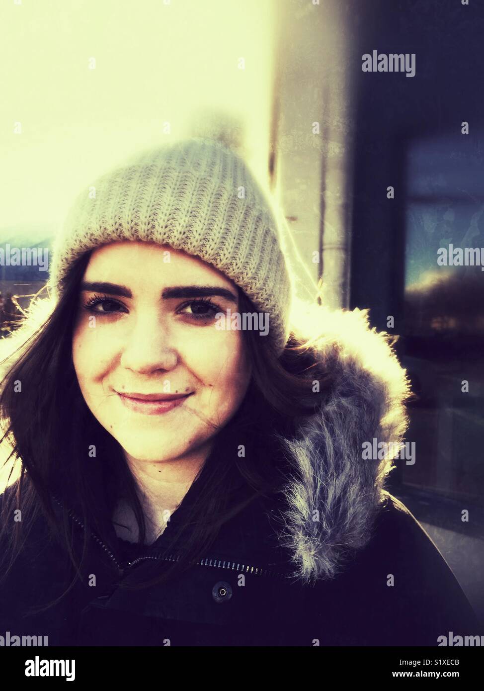 Smiling young woman in wool hat and parka outside. Stock Photo