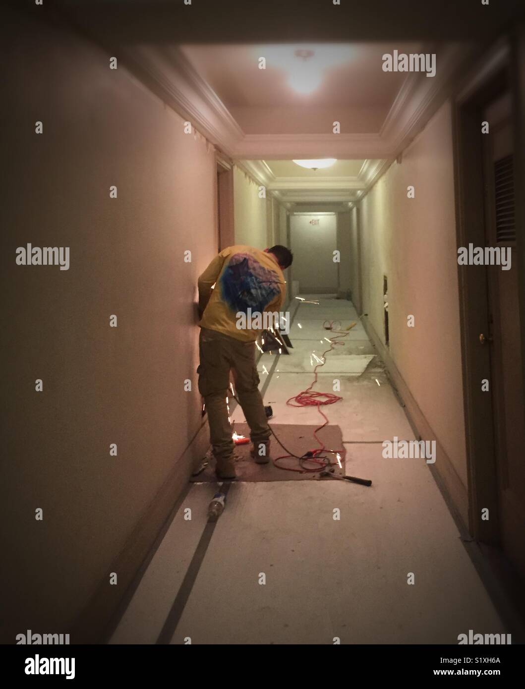 Worker using steel grinder tool in co-op apartment building hallway renovation, New York City, USA - Smartphone Captured Stock Image