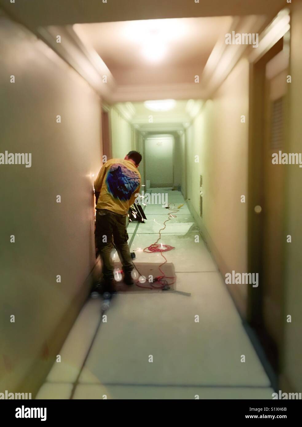 Worker using steel grinder tool in apartment building hallway renovation, New York City, USA - Smartphone Captured Stock Image