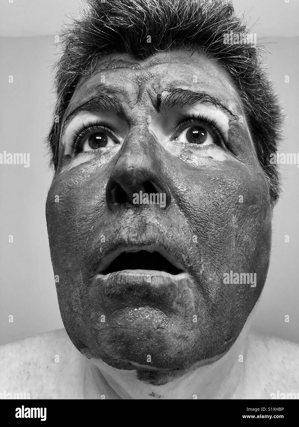 A black and white close up portrait of a woman wearing a mud mask with a shocked expression Stock Photo