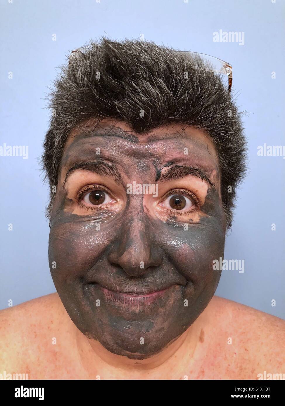 A portrait of a dark haired Caucasian woman wearing a mud mask and smiling - Smartphone Captured Stock Image