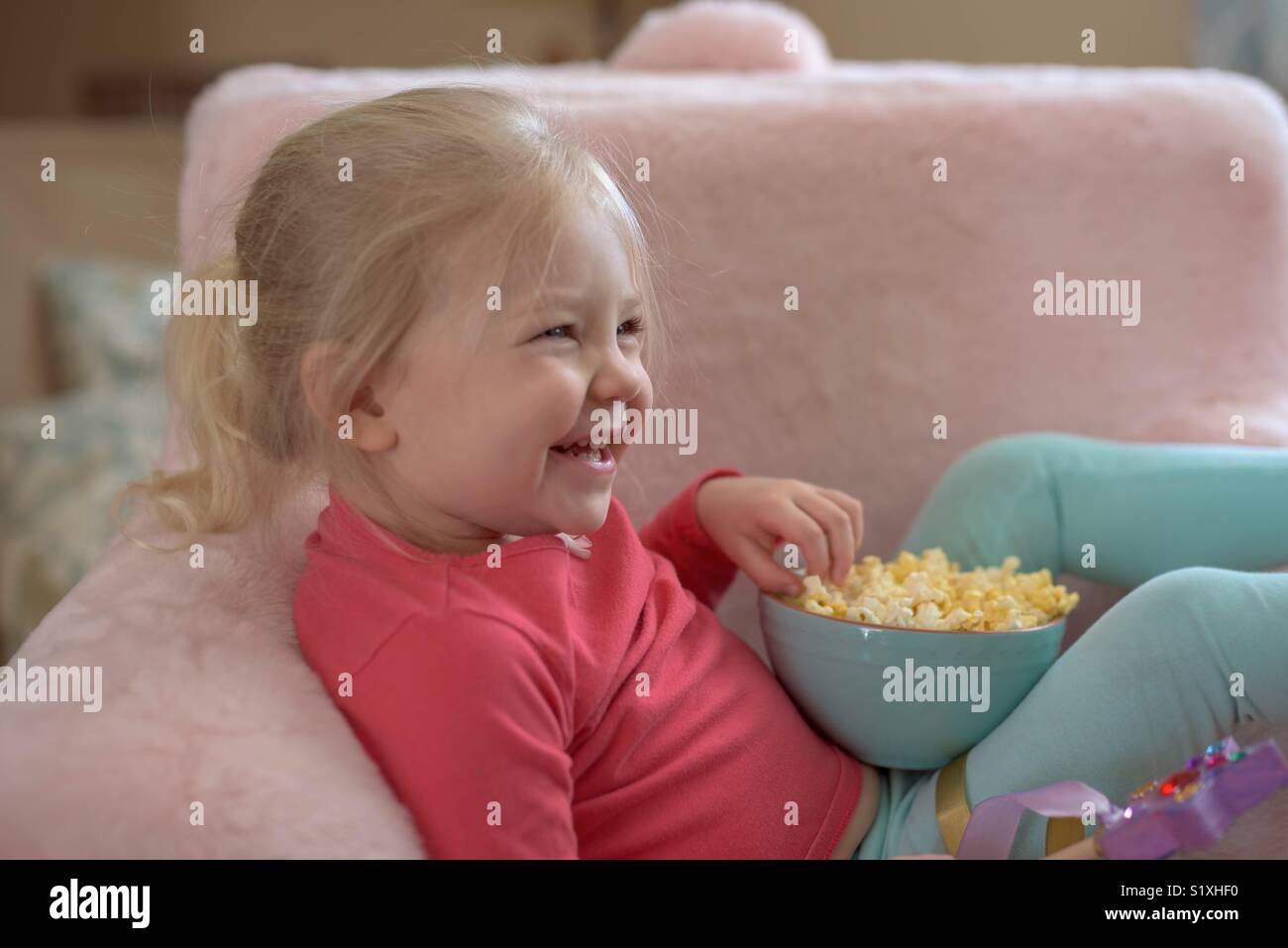 Smiling child eating popcorn while watching a movie on TV Stock Photo