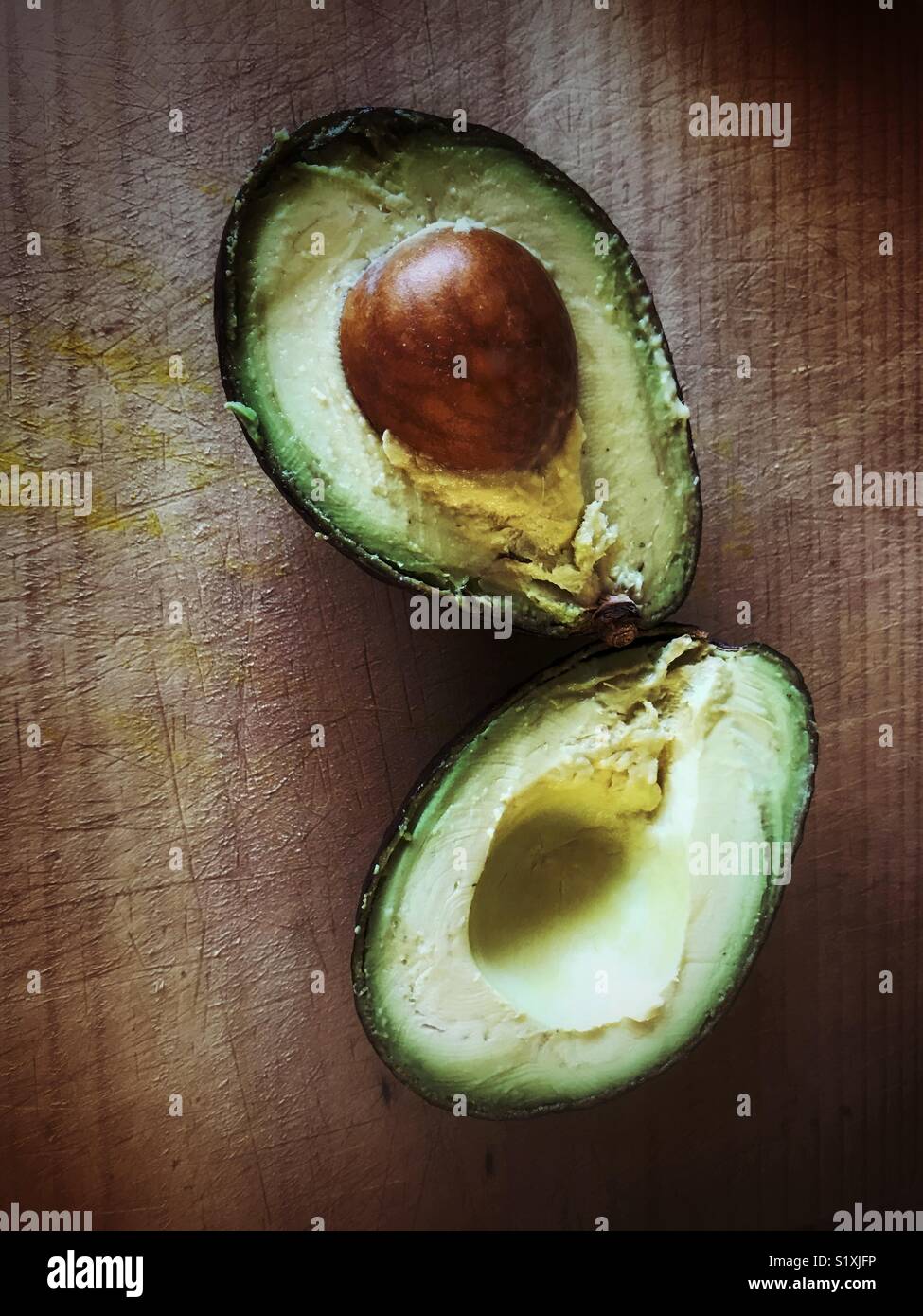 Overhead shot of an avocado cut in half on a cutting board. Stock Photo