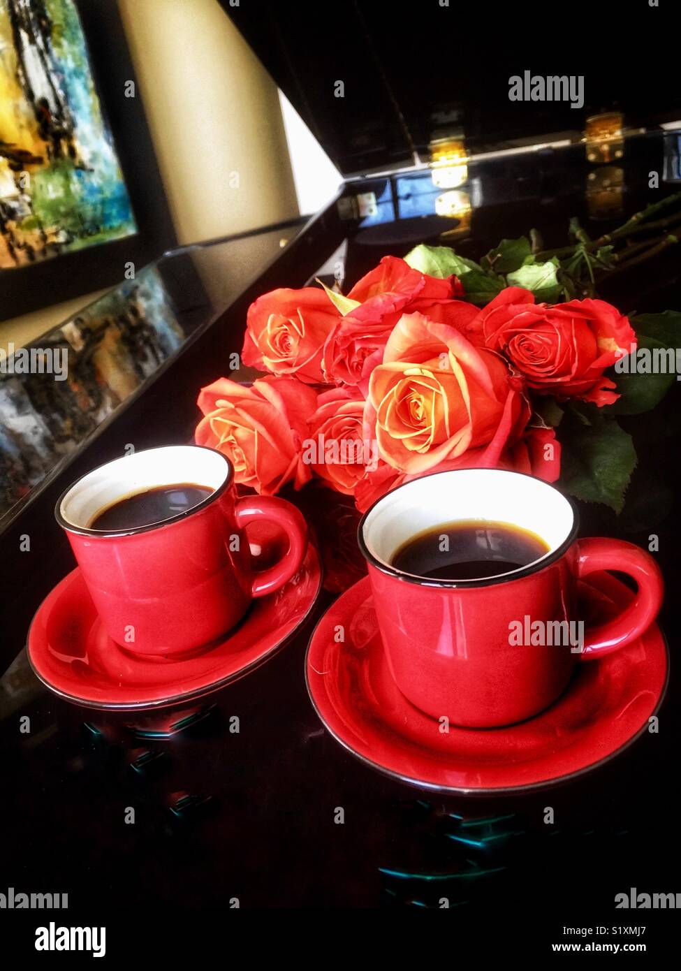 Two expresso cups with red saucers and red roses laying on black baby grand piano Stock Photo