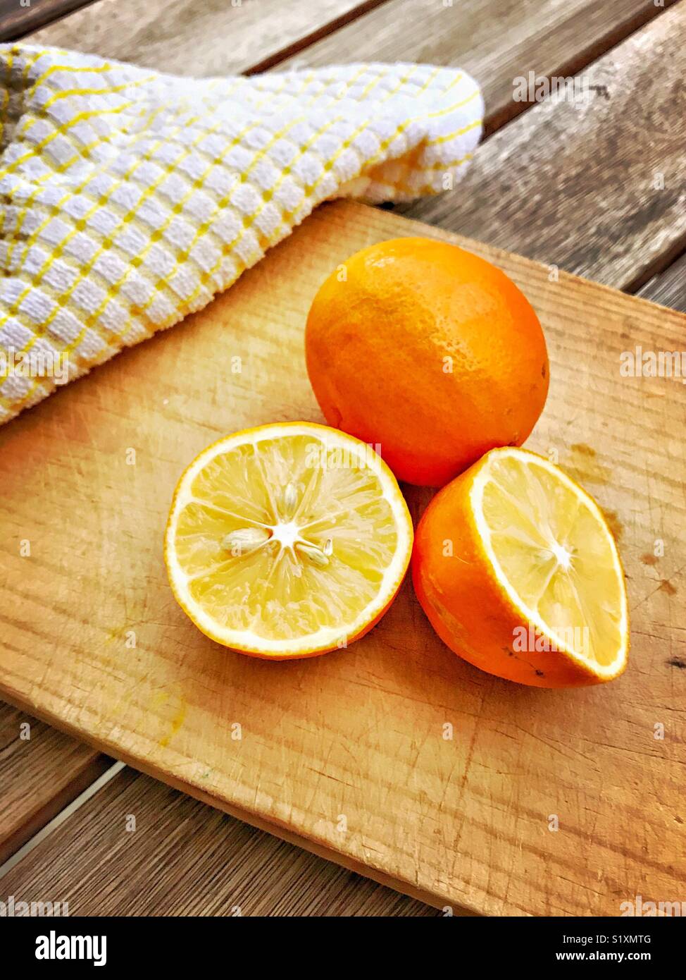 Orange skinned lemons are displayed on a cutting board showing both the whole lemon and one cut in half. Stock Photo