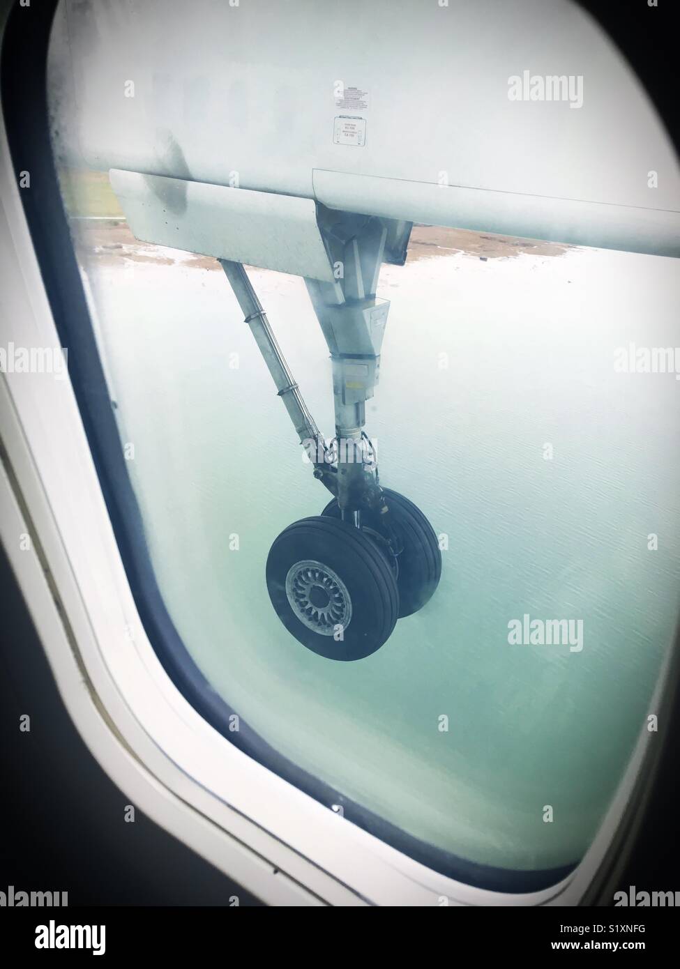 View out of an airplane window, looking at airplane tires approaching landing over water. - Smartphone Captured Stock Image