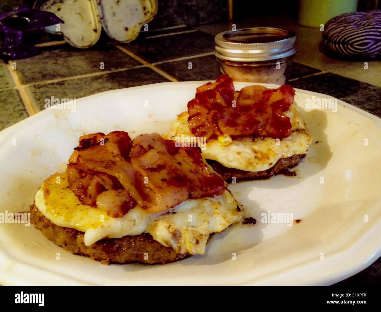 Hamburgers, eggs, and bacon on white plate, with jar of Himalayan salt - Smartphone Captured Stock Image