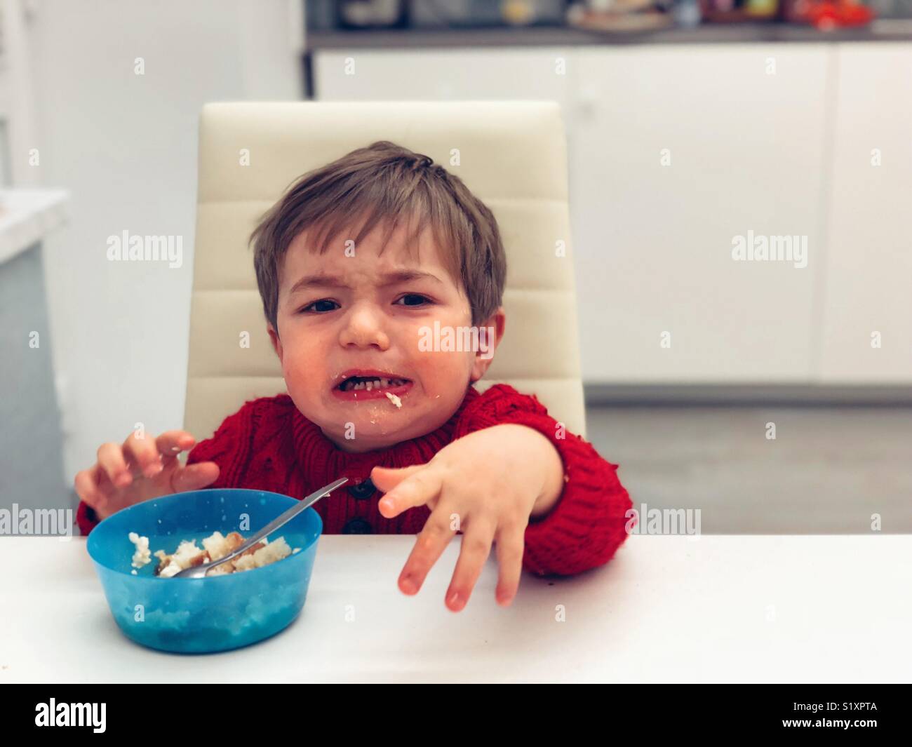 Unhappy baby boy eating by himself Stock Photo