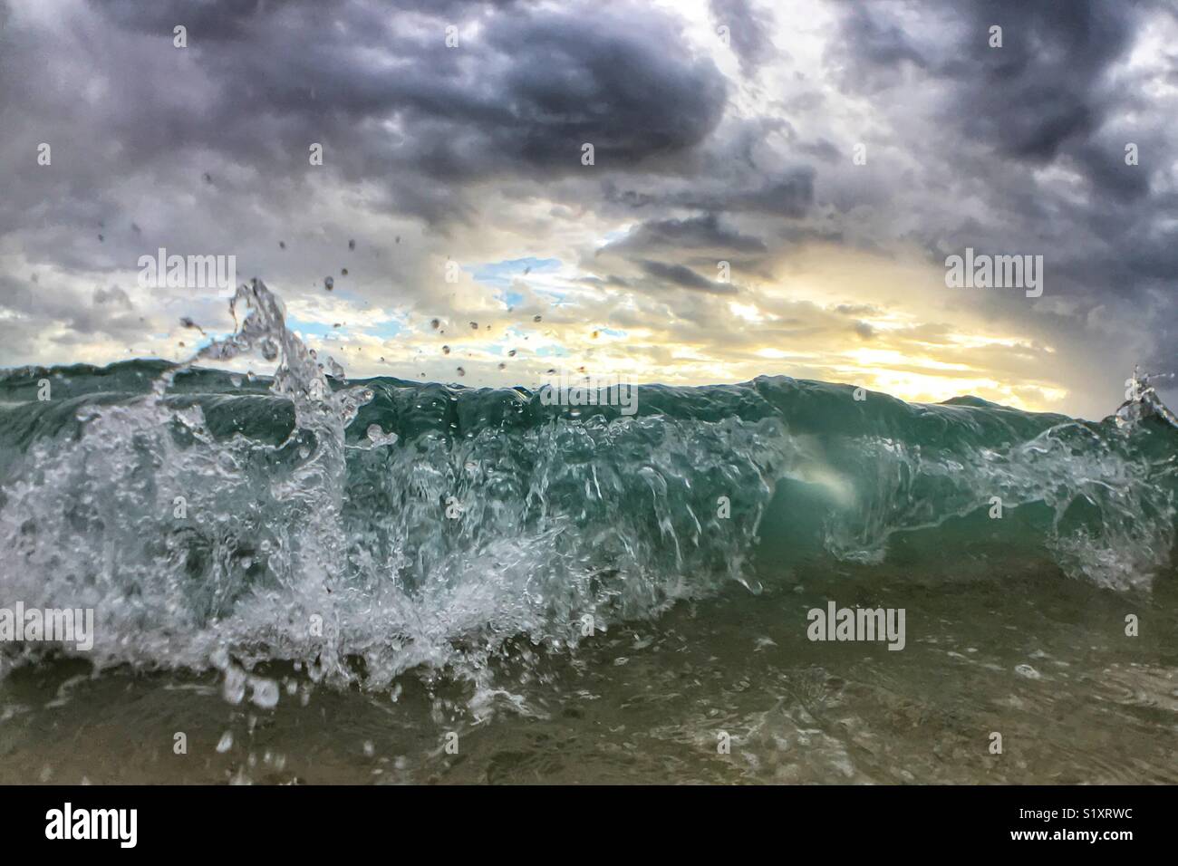 Ocean and sky. Close up of a wave curling with overcast sunset above. Stock Photo