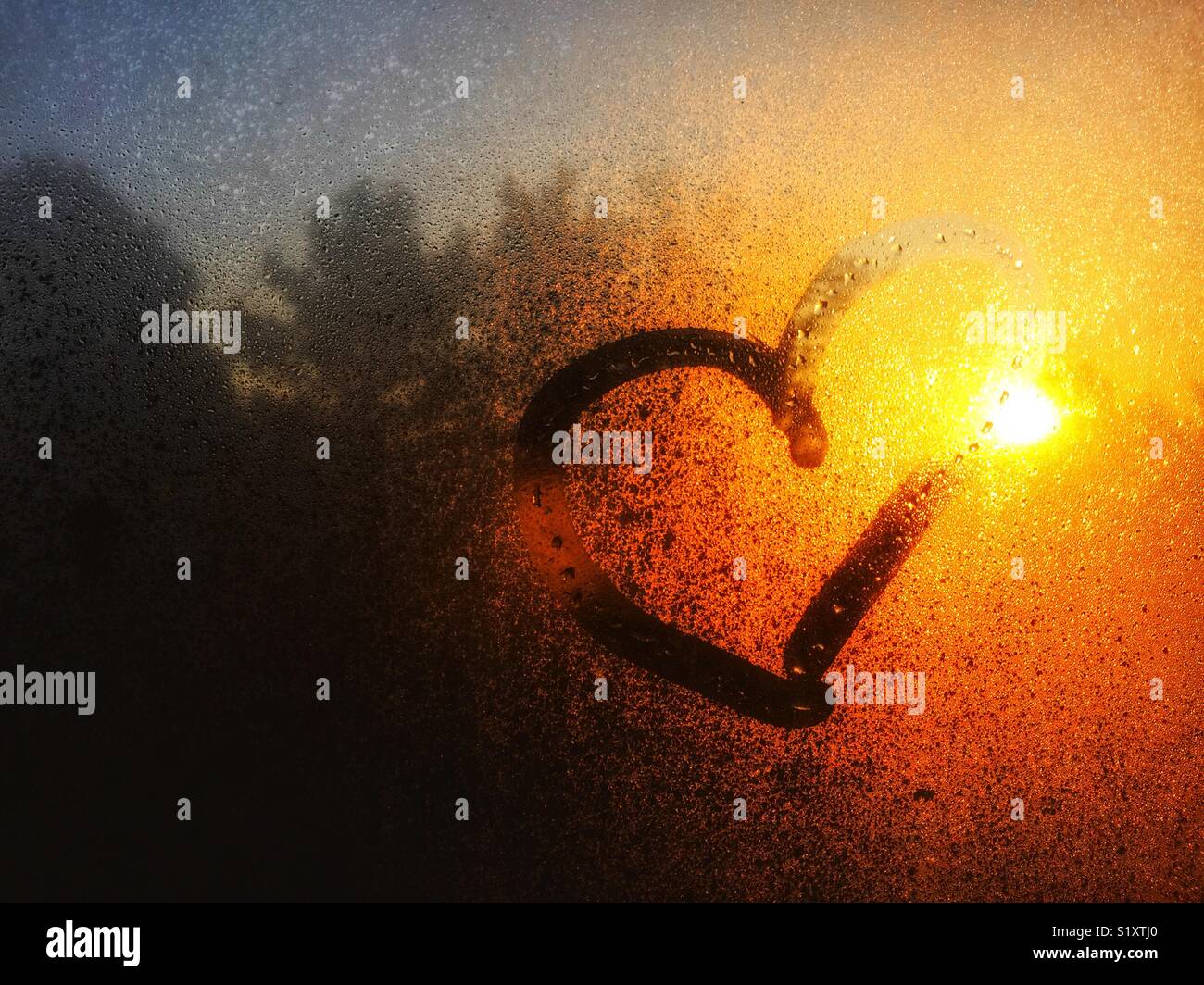 Morning sunlight on through condensed water on window with a heart drawn on it Stock Photo