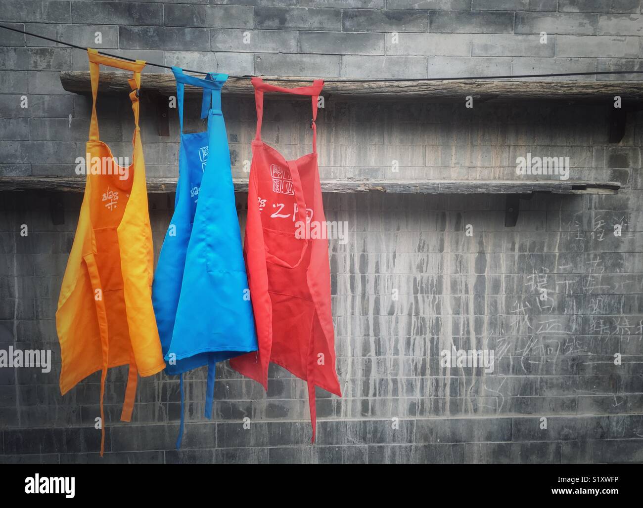 Three colorful aprons hanging on a line against grey brick wall - Smartphone Captured Stock Image