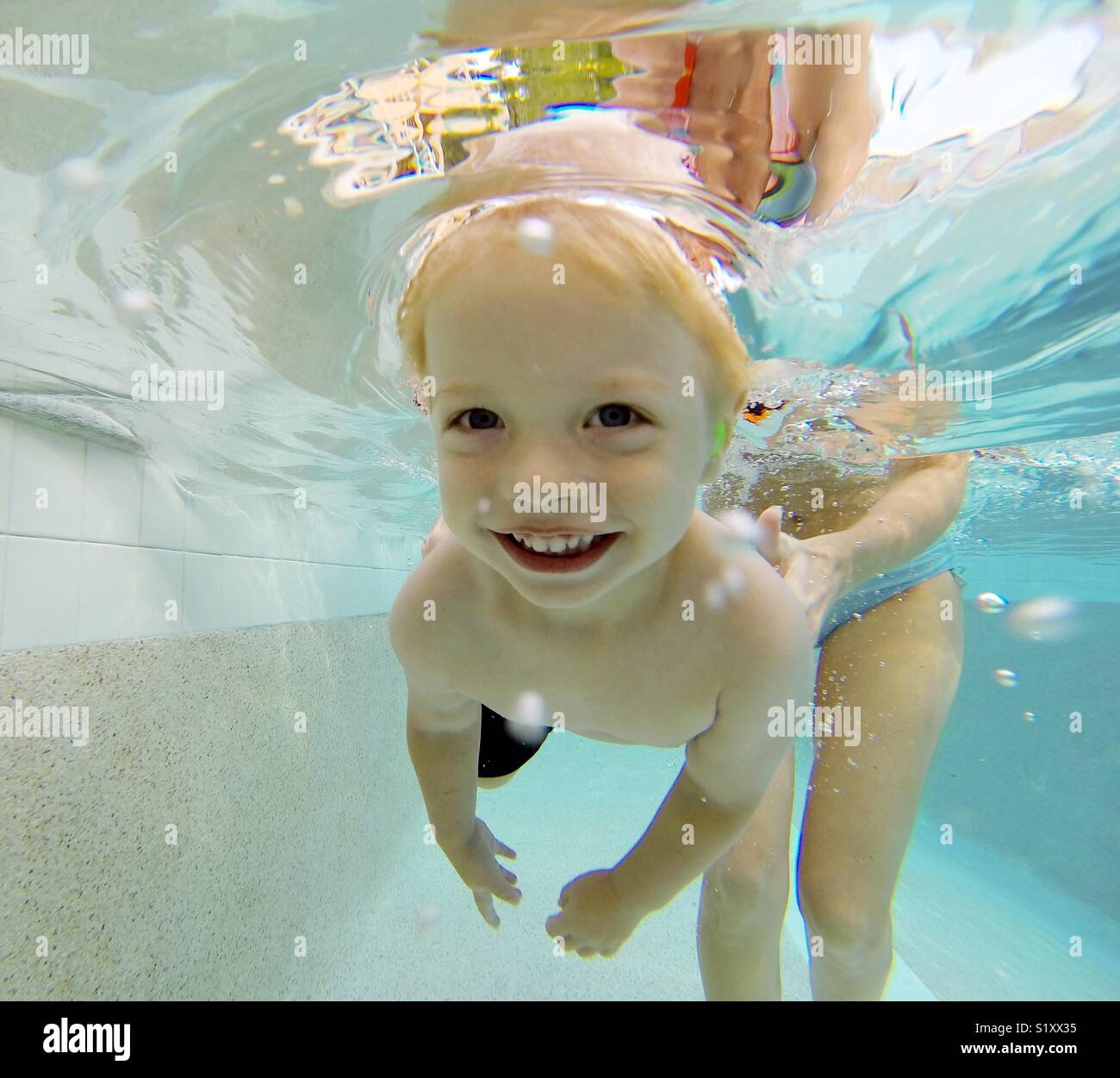 A boy smiles as he swims underwater with his eyes open in a swimming