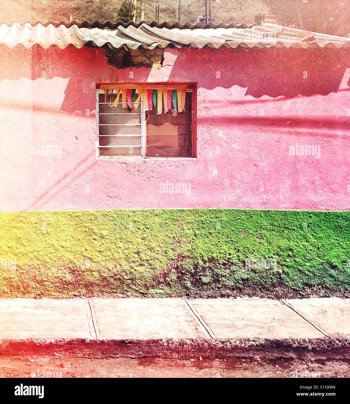 Colorful streamers hang from an eye catching window in a pink and green wall on a street in Ajijic, Mexico. Stock Photo