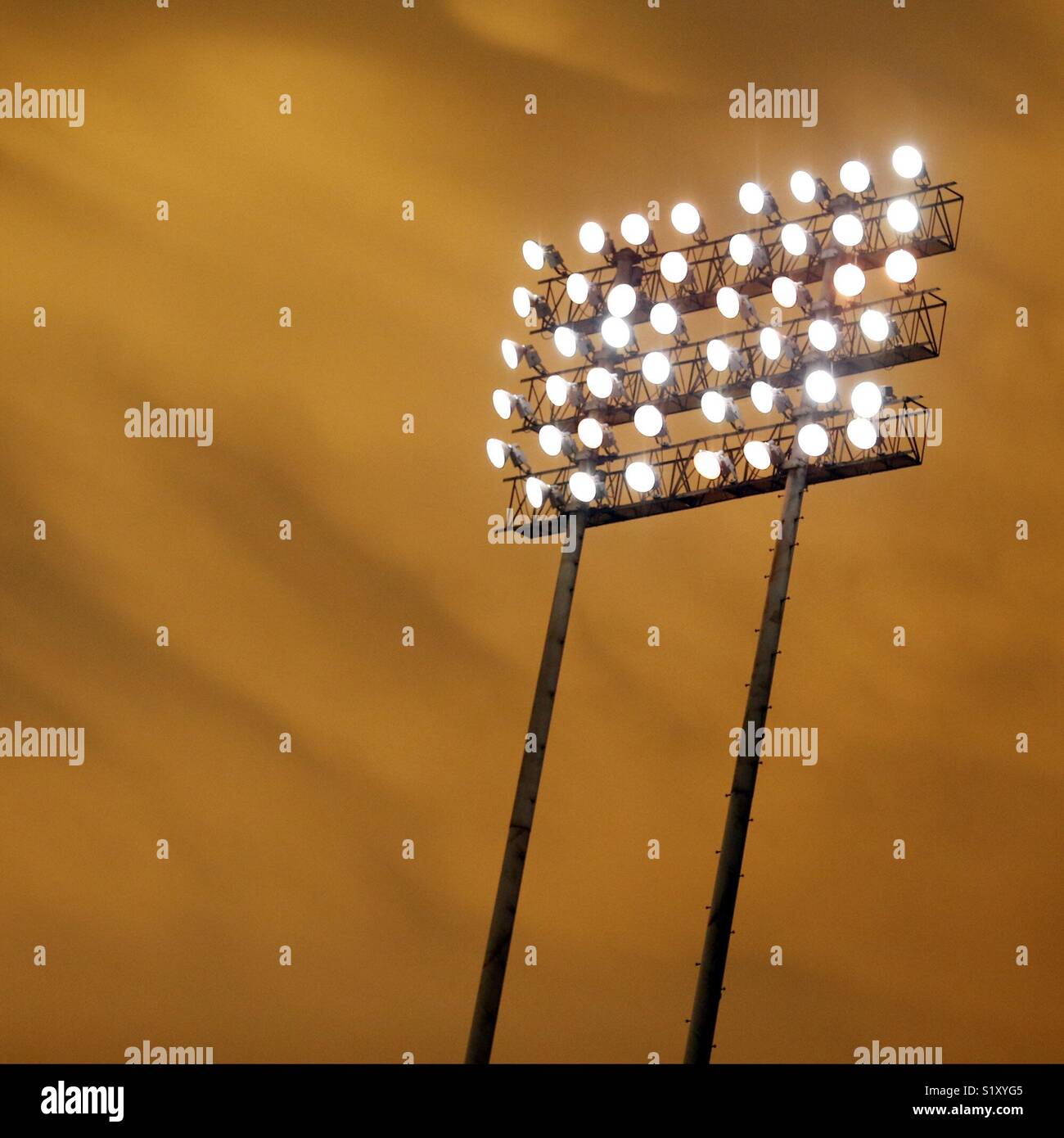 Stadium lights are illuminated against an orange sunset sky. - Smartphone Captured Stock Image