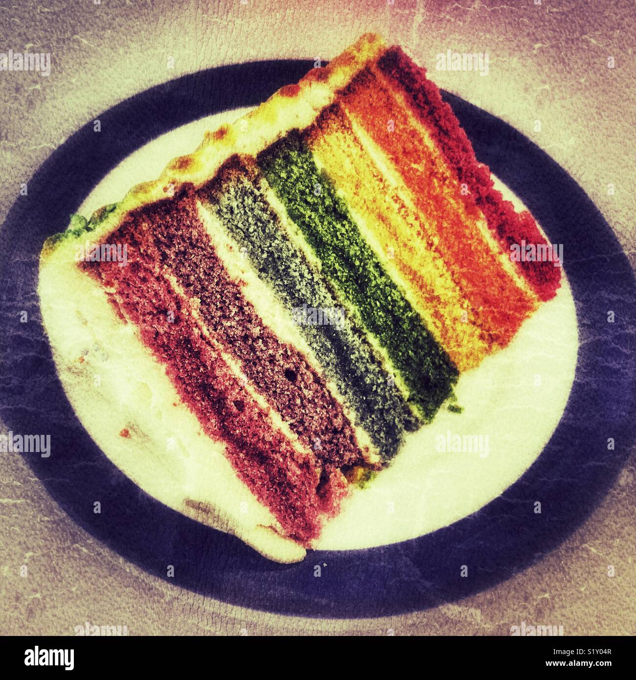 Slice of freshly baked, iced, rainbow cake on a blue rimmed plate - Smartphone Captured Stock Image