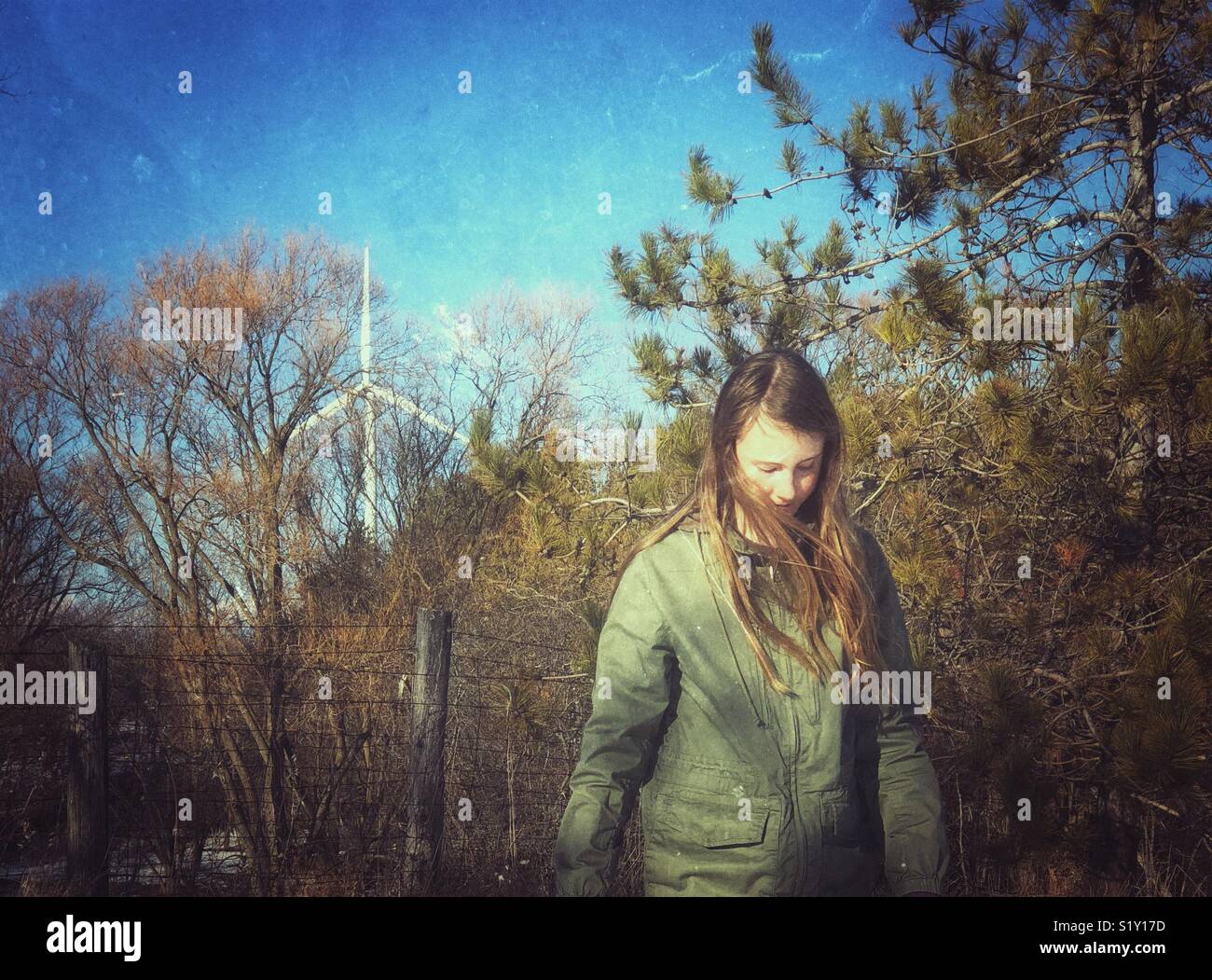 Girl walking outside looking down with trees and wind turbine in background - Smartphone Captured Stock Image