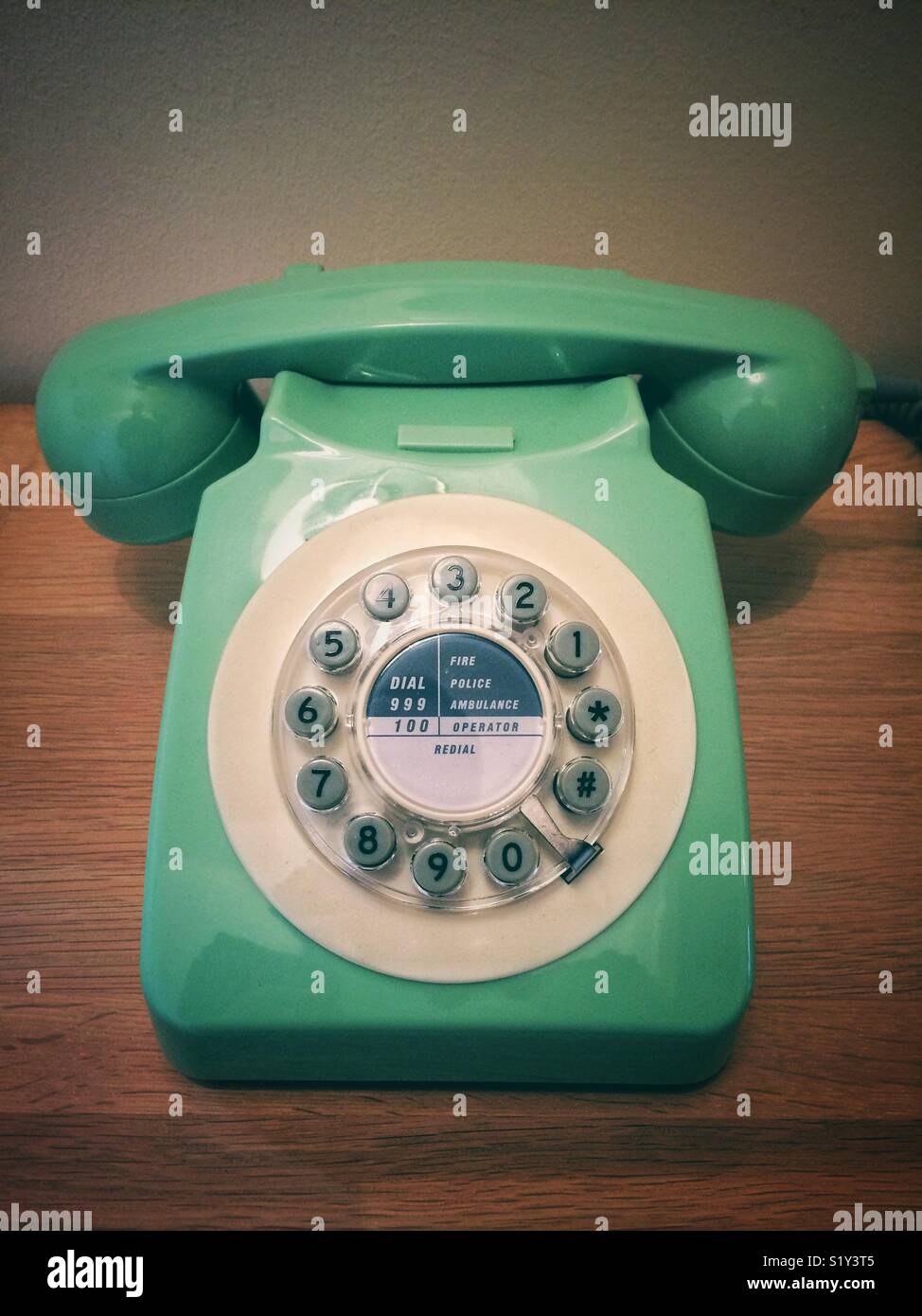 An old fashioned, retro style telephone with handset and circular dial in green and on a wooden background - Smartphone Captured Stock Image